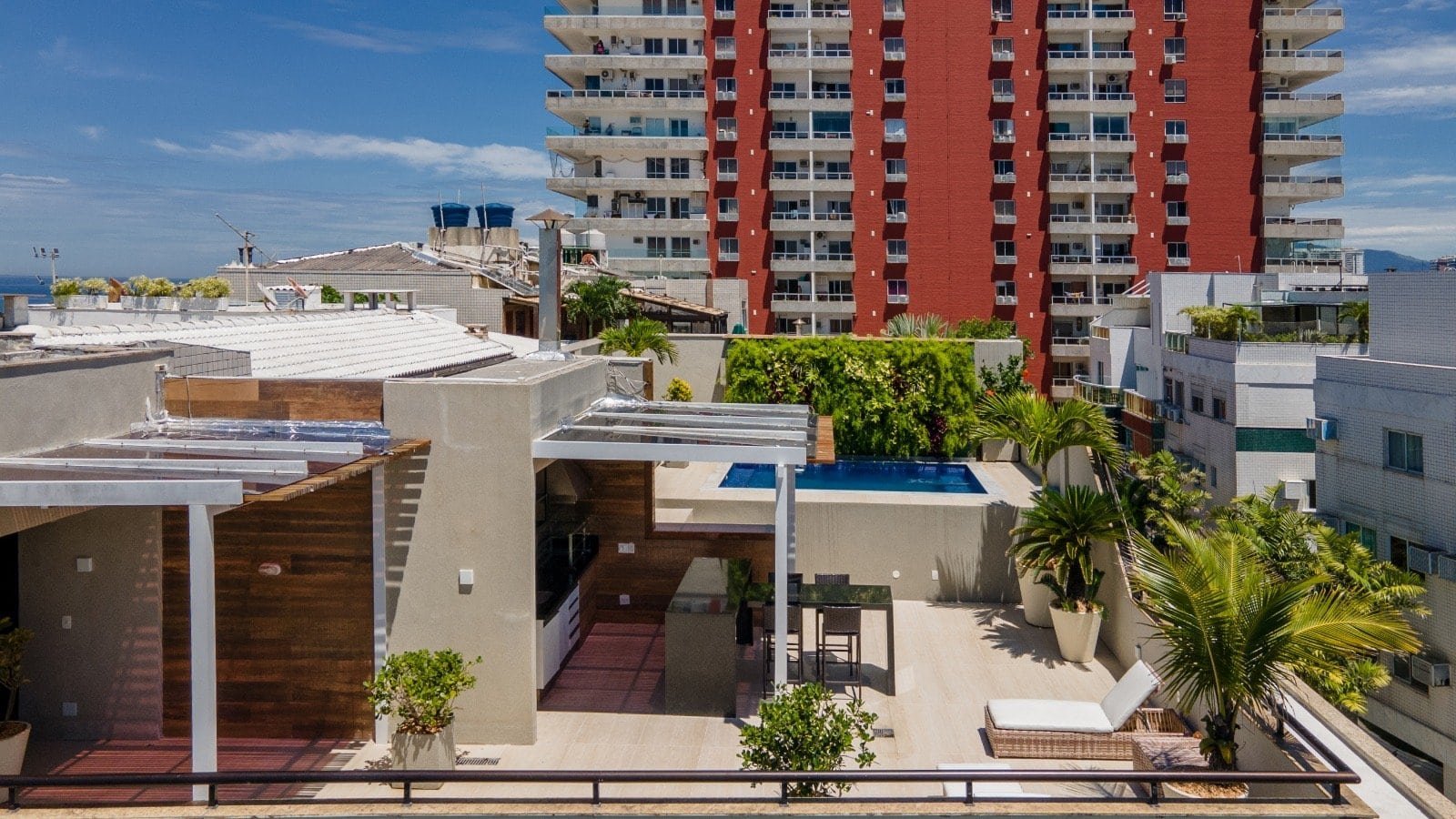 Lavanderia e espaço ao ar livre no rooftop de edifício residencial em Praia Grande, São Paulo, com vista urbana, piscina, plantas tropicais e área de convivência moderna.