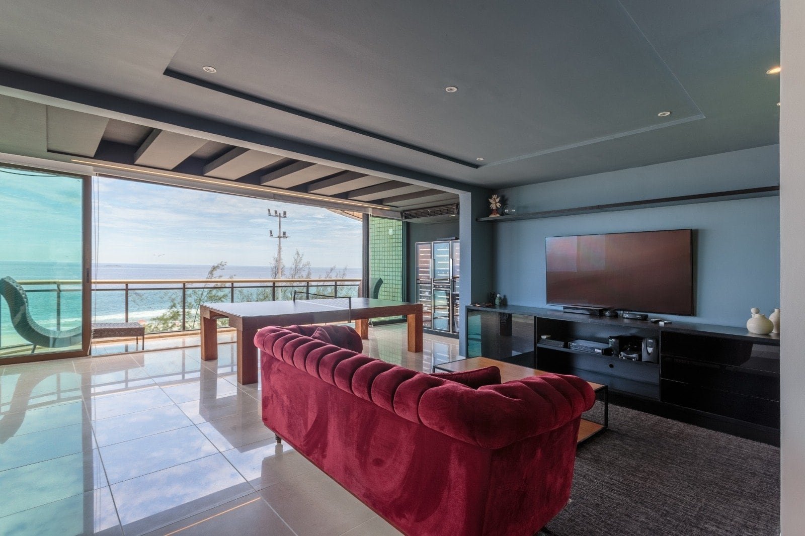 Lobby do apartamento de frente para o mar com vista deslumbrante, sofá vermelho, televisão, móveis modernos e varanda com vista panorâmica do oceano, perfeito para relaxar e apreciar o pôr do sol.