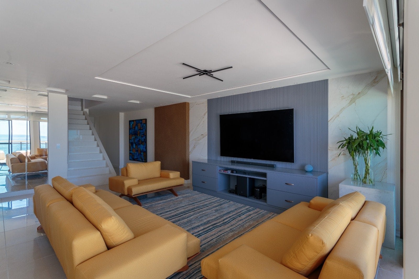 Conjunto de sofás amarelos em sala de estar moderna com TV de alta tecnologia, detalhes em mármore e plantas decorativas, ideal para residências de alto padrão e projetos de design de interiores sofisticados.