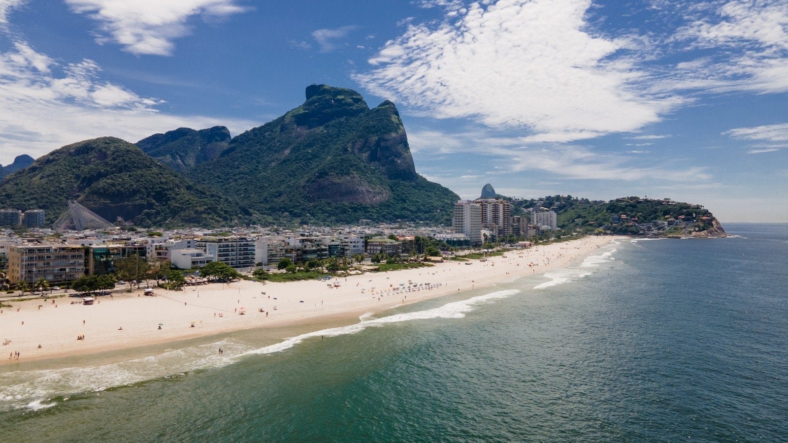 Praia de Copacabana com vista para os morros do Pão de Açúcar e do Corcovado, cenário icônico do Rio de Janeiro, com areia branca, mar azul e urbanização ao fundo, perfeito para turismo e lazer.
