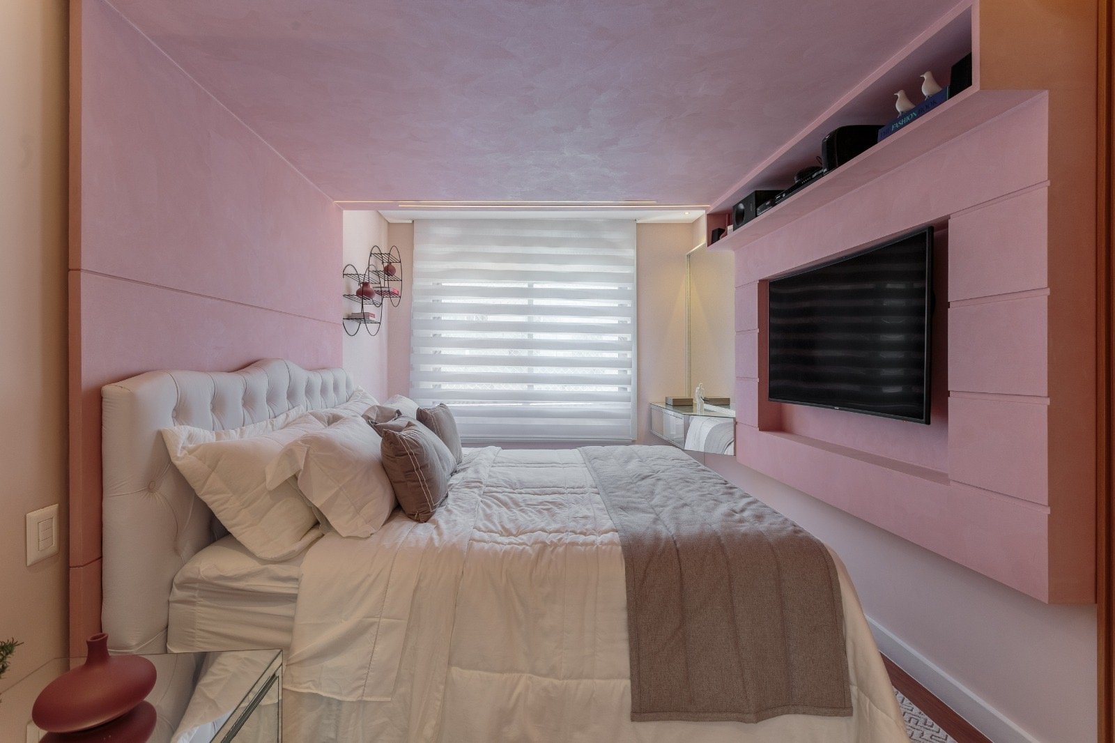 Confortável suíte moderna com decoração elegante, televisão de tela gigante e detalhes em rosa, ideal para hotéis de luxo, com móveis sofisticados e iluminação aconchegante.
