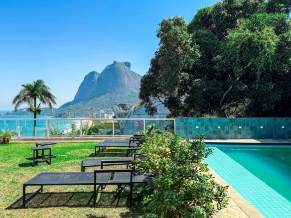 Piscina de luxo com uma vista deslumbrante do Morro do Pão, área lounge ao ar livre com espreguiçadeiras e jardins bem cuidados em uma residência da Gruppo Monaco em local privilegiado.