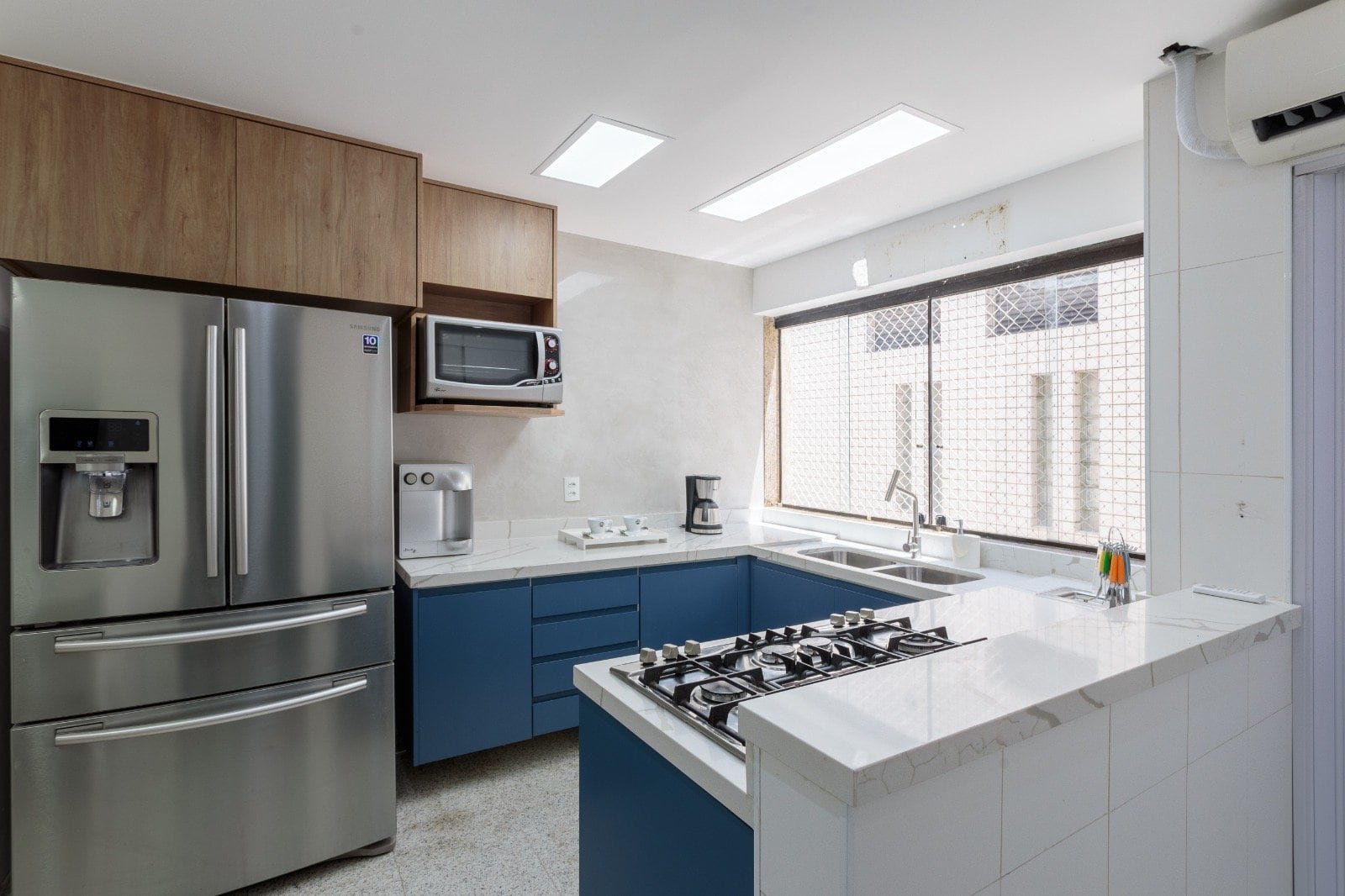 Reforma de cozinha moderna com armários azuis e brancos, eletrodomésticos integrados, amplo espaço e iluminação natural. Ideal para residências contemporâneas em Curitiba.