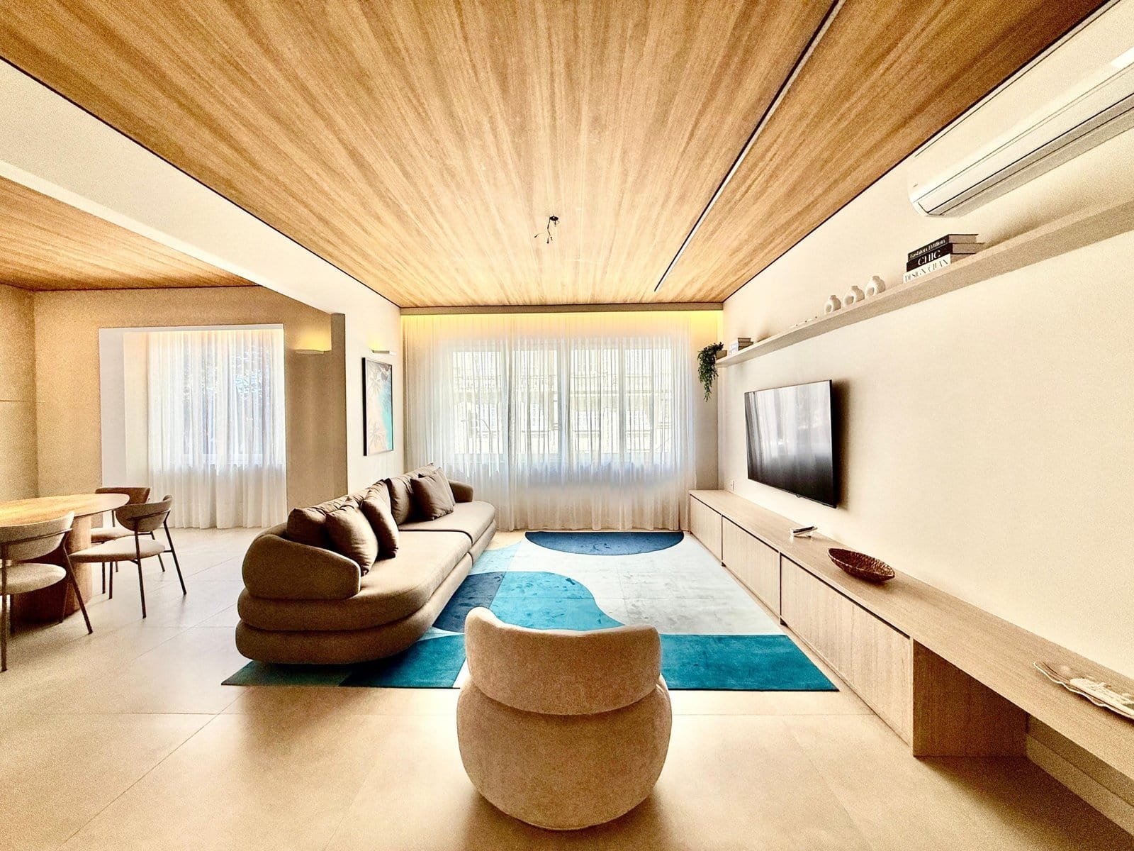 Modern living room with contemporary furniture, neutral tones, wooden ceiling, and large windows with sheer curtains, highlighting elegant interior design and cozy ambiance.