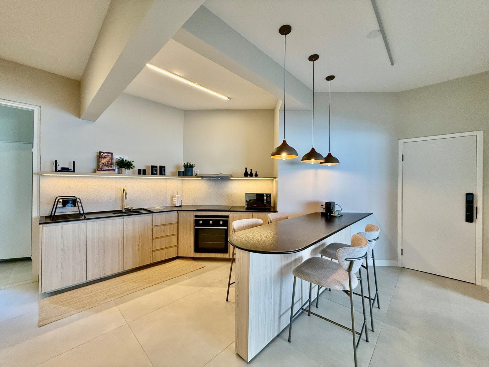Moderno espaço de cozinha com balcão de café da manhã, iluminação suave e móveis de acabamento claro, criando ambiente aconchegante e funcional, ideal para residências sofisticadas.