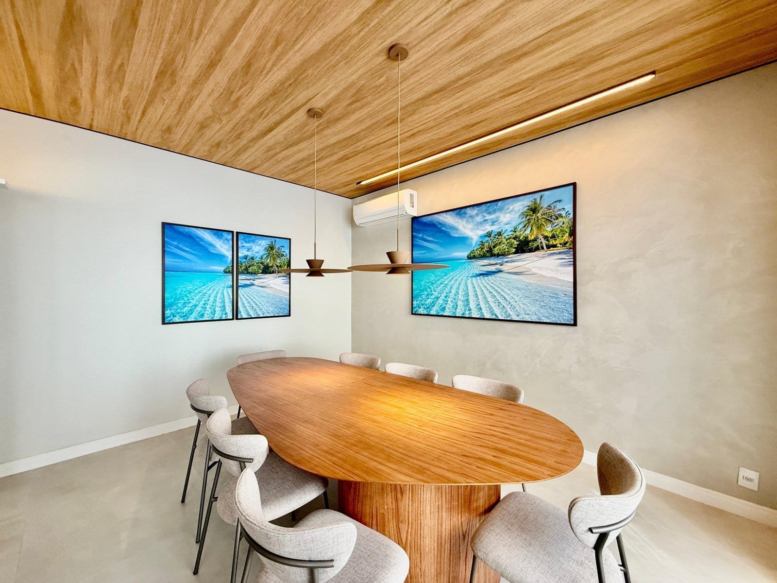 Imagem de uma sala de reunião moderna com mesa de madeira oval e oito cadeiras confortáveis, decorada com dois grandes quadros de paisagem praiana e teto de madeira, transmitindo sofisticação e elegância.