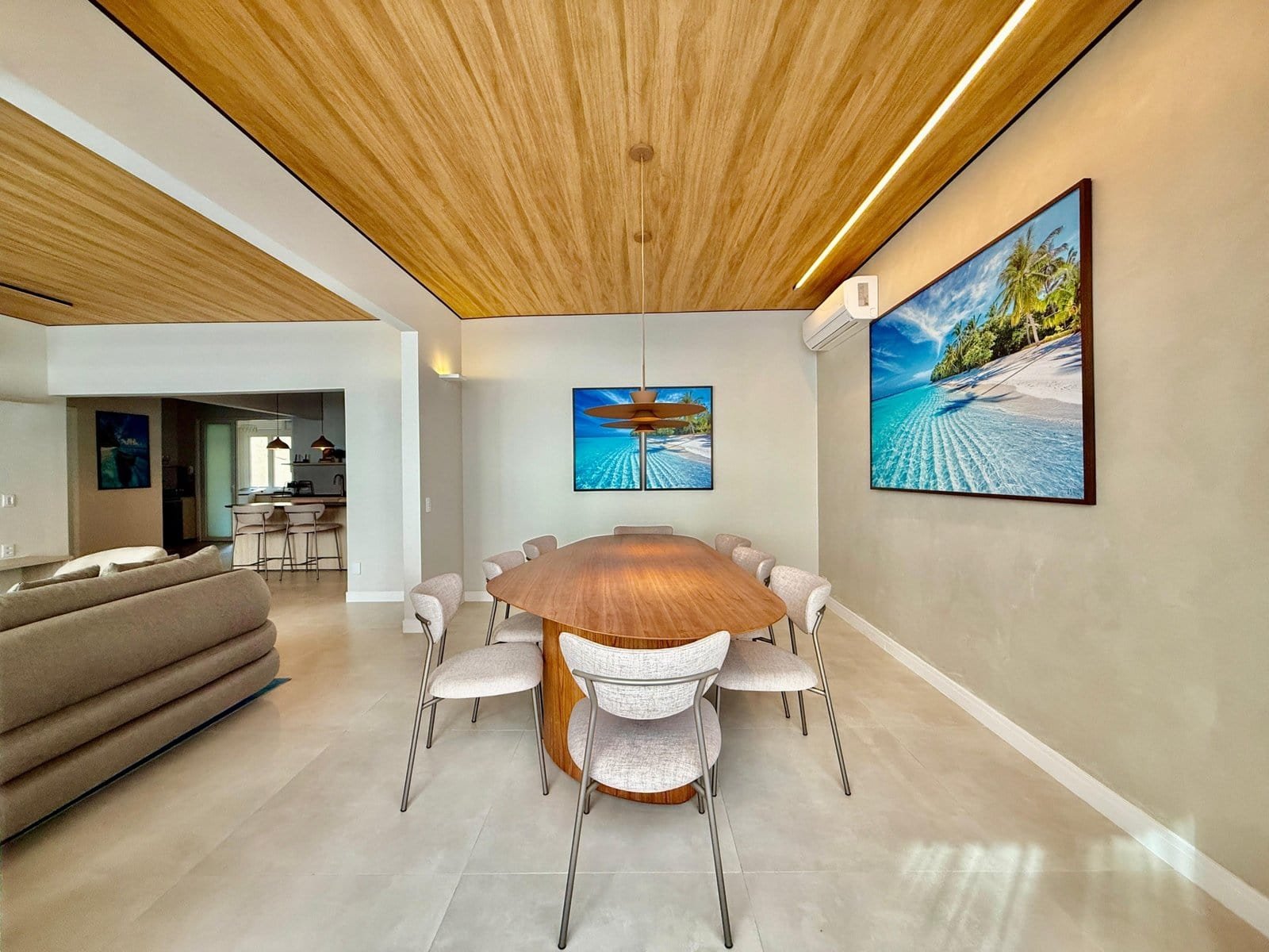 Linda sala de jantar com decoração moderna e painel de arte com tema praia, móveis elegantes em tom neutro, piso de porcelanato e detalhes em madeira na cobertura do teto, ideal para ambientes sofisticados.