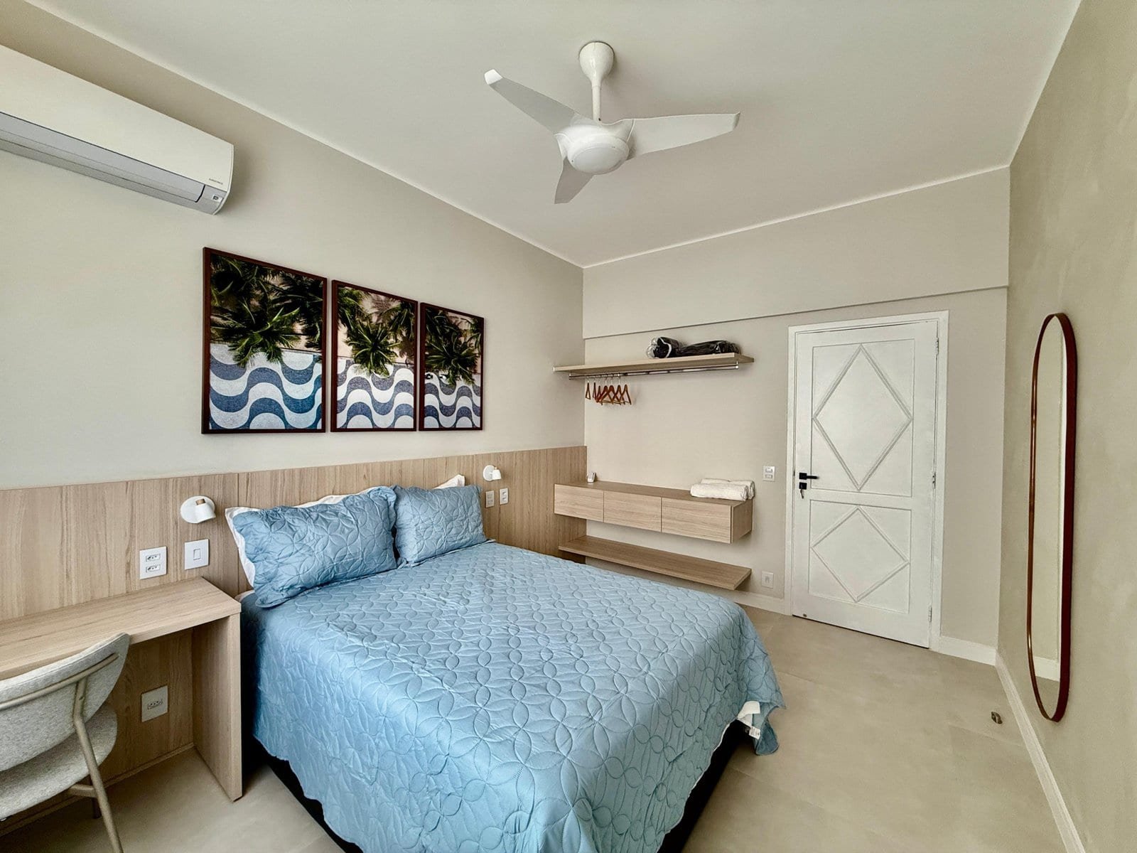 Conjunto de imagens de um quarto de hotel com decoração moderna e minimalista, cama de casal com roupa de cama azul, quadros decorativos na parede, televisão, ar-condicionado e espelho de corpo inteiro, proporcionando conforto e elegância.