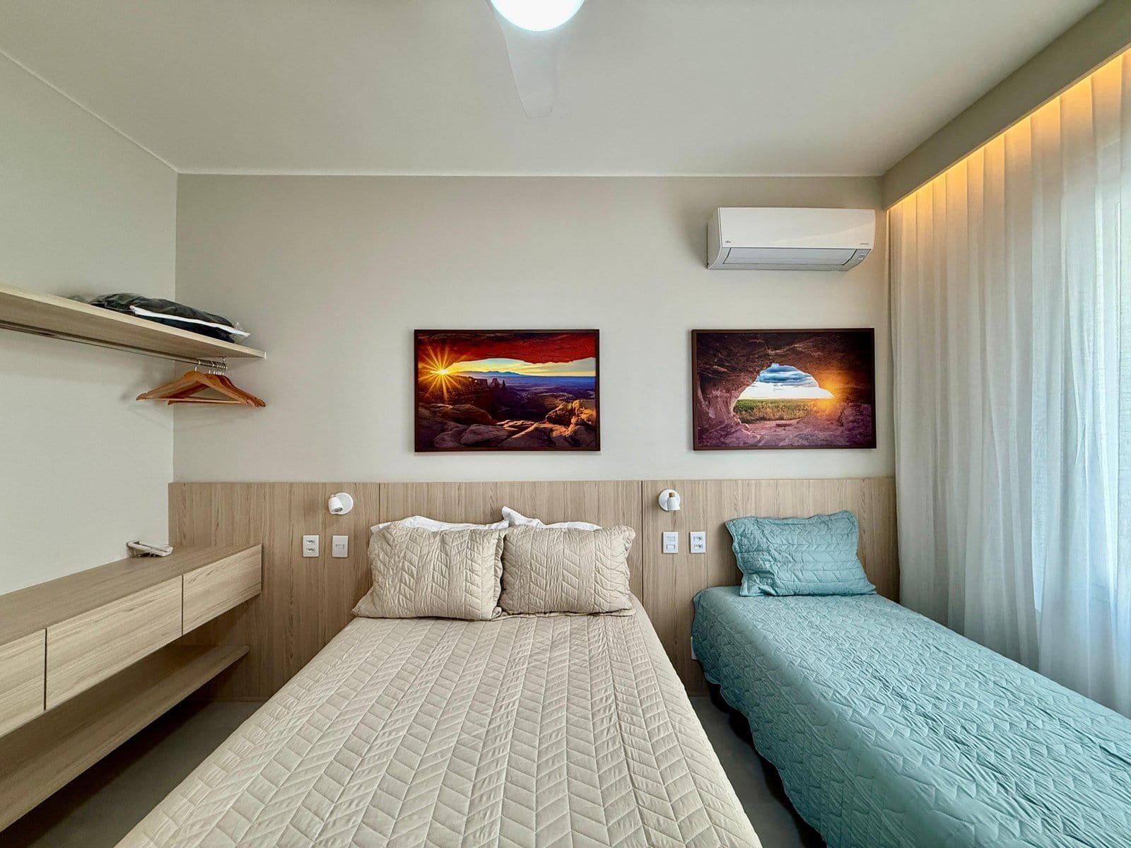 Luminária de teto moderna no quarto com duas camas, decoração minimalista, quadros com paisagens naturais e ar-condicionado, ambiente confortável e bem iluminado para uma estadia agradável.