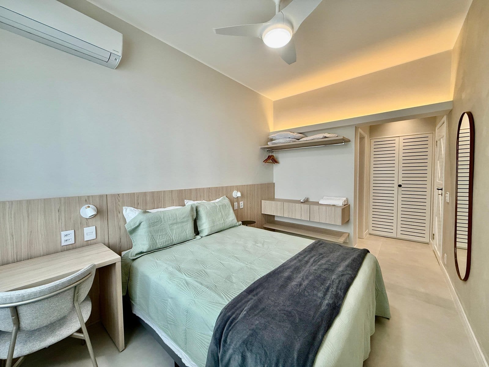 Confortável quarto de hotel com cama king size, decoração moderna em tons neutros, ar-condicionado, iluminação aconchegante, armários embutidos, espelho, e espaço bem organizado para uma estadia agradável.