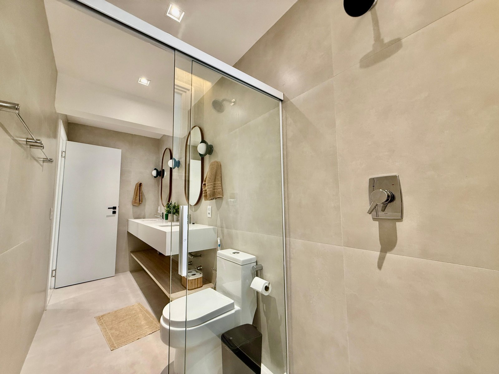 Luxo e funcionalidade em banheiro moderno com revestimentos elegantes, painel de espelho, ducha de livre acesso, vaso sanitário confortável, detalhes em decoração neutra e iluminação eficiente, ideal para residências sofisticadas.