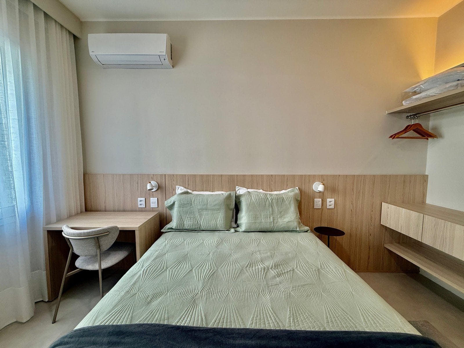 Quarto de hotel elegante com cama de casal, decoração moderna, ambiente confortável, móveis de madeira clara, ar-condicionado, iluminação suave e janelas com cortinas de tecido branco para descanso perfeito.