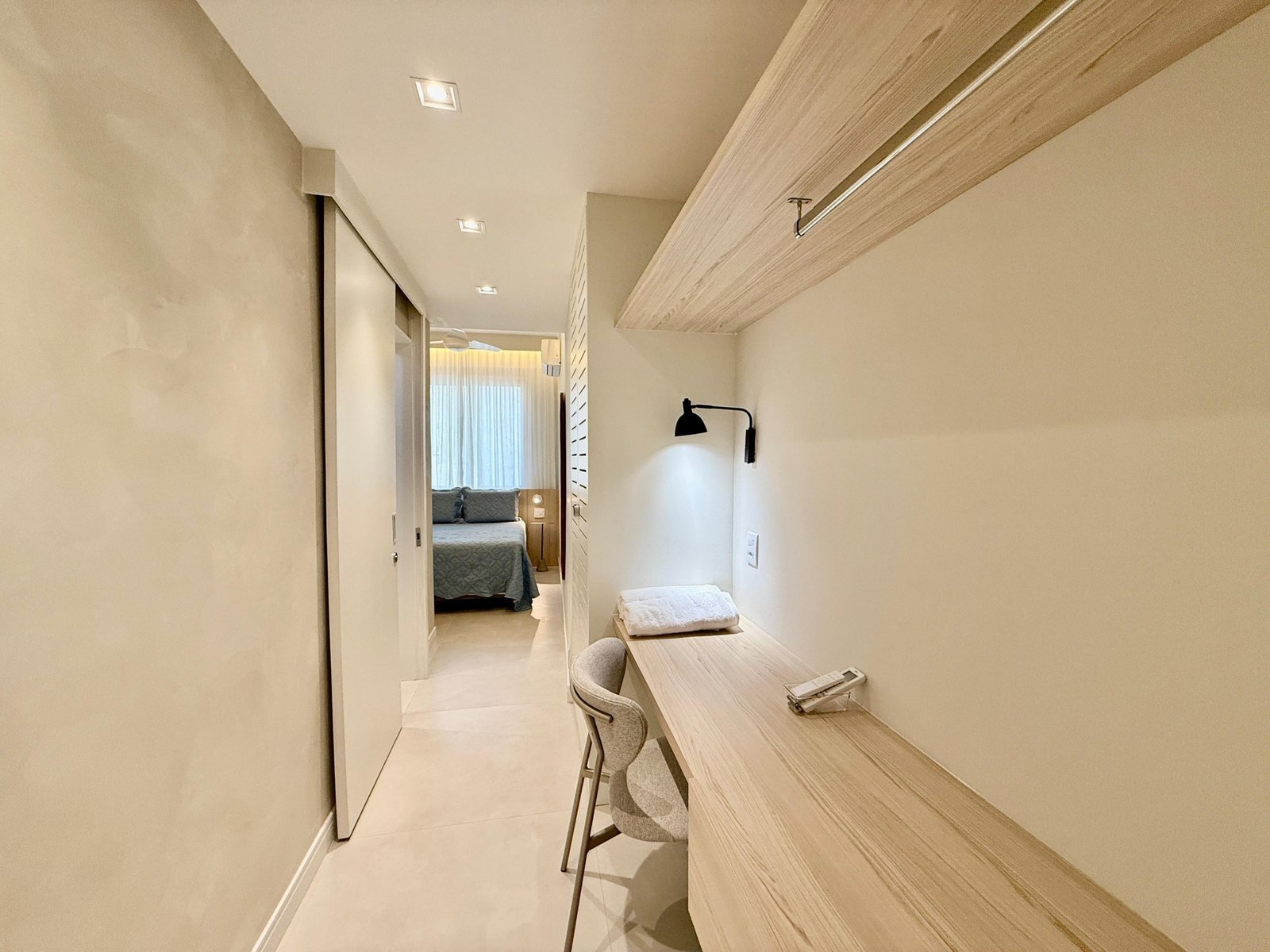Meta: escritório compacto com bancada de madeira, iluminação discreta e área de descanso com vista para o quarto. Ambientes modernos e funcionais, ideais para trabalho e relaxamento no hotel Grupo Monaco.