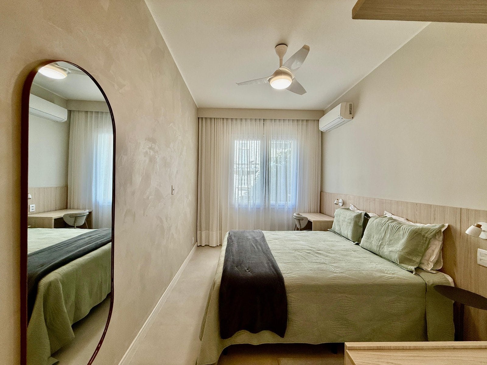 Luxo em quarto de hotel com cama king size, decoração moderna, ar-condicionado split, iluminação suave e janelas com cortinas translúcidas para uma estadia confortável.