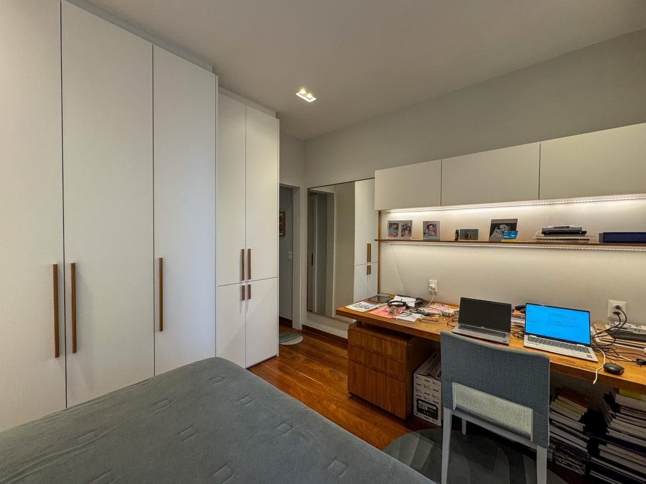 Armário planejado branco com detalhes em madeira, espaço de estudo com computador, livros e objetos pessoais, ambiente organizado e moderno na decoração de interiores.