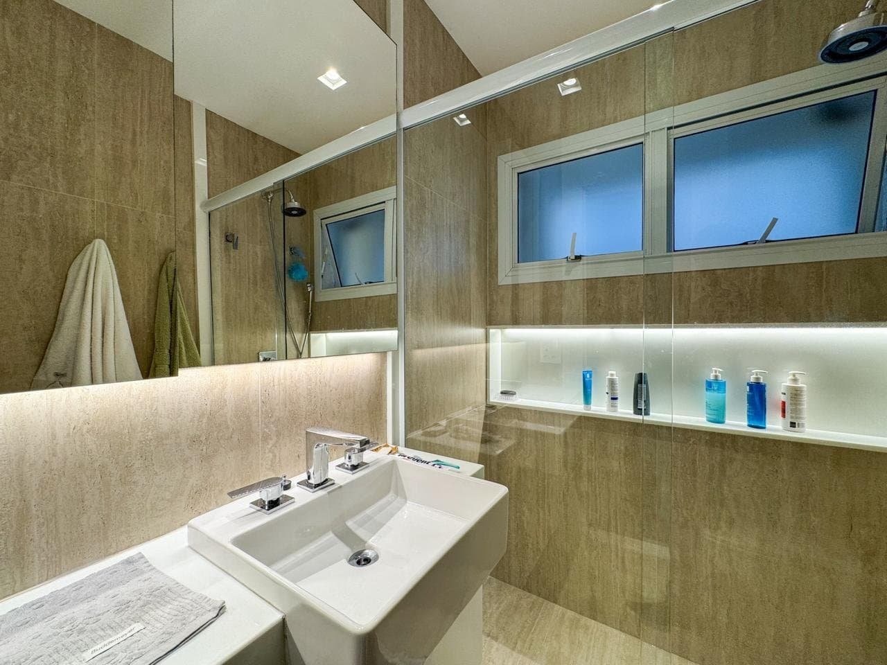 Luxo em banheiro moderno com espelho grande, torneiras duplas e detalhes em madeira, iluminação embutida e azulejos de alta qualidade, refletindo elegância e funcionalidade para ambientes residenciais e comerciais.