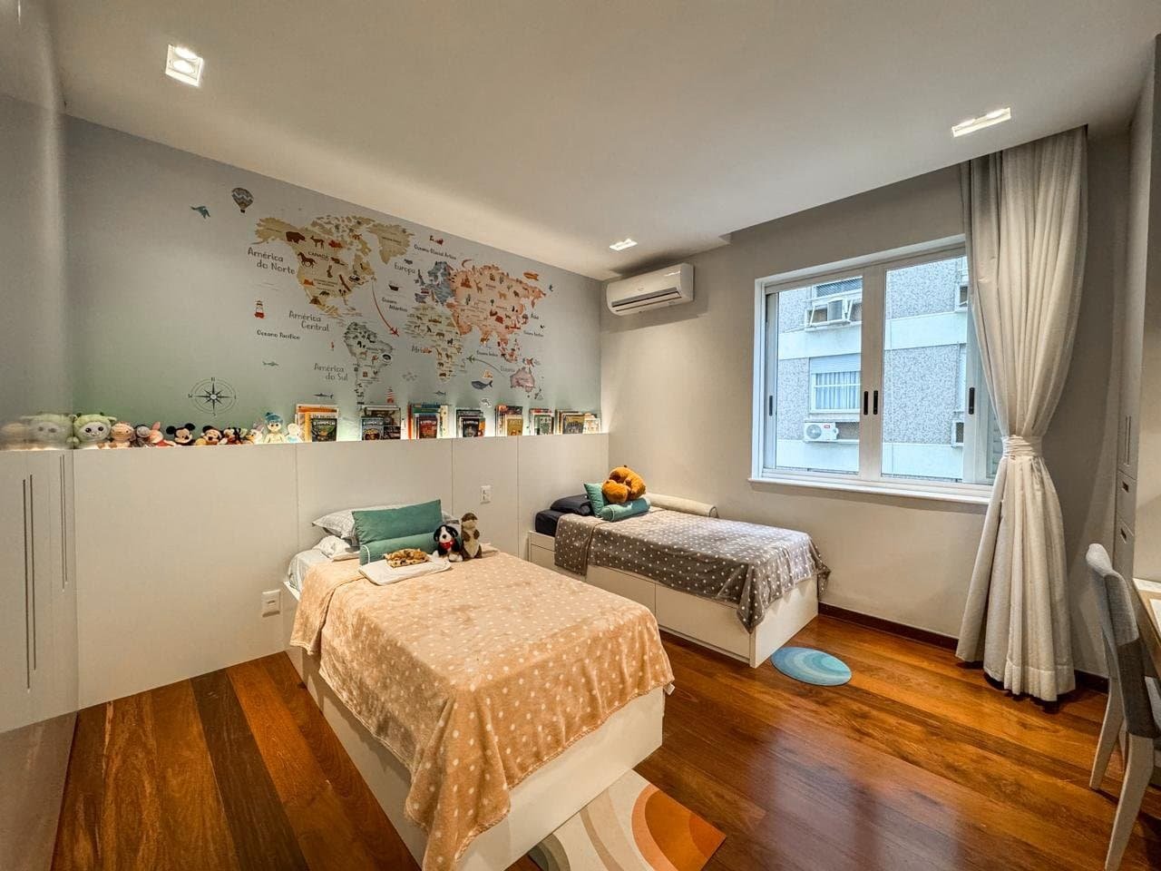 Imagem de quarto infantil decorado com tema de aventura e viagem, com mapa-múndi na parede e brinquedos ao redor das camas, promovendo conforto e criatividade para crianças.