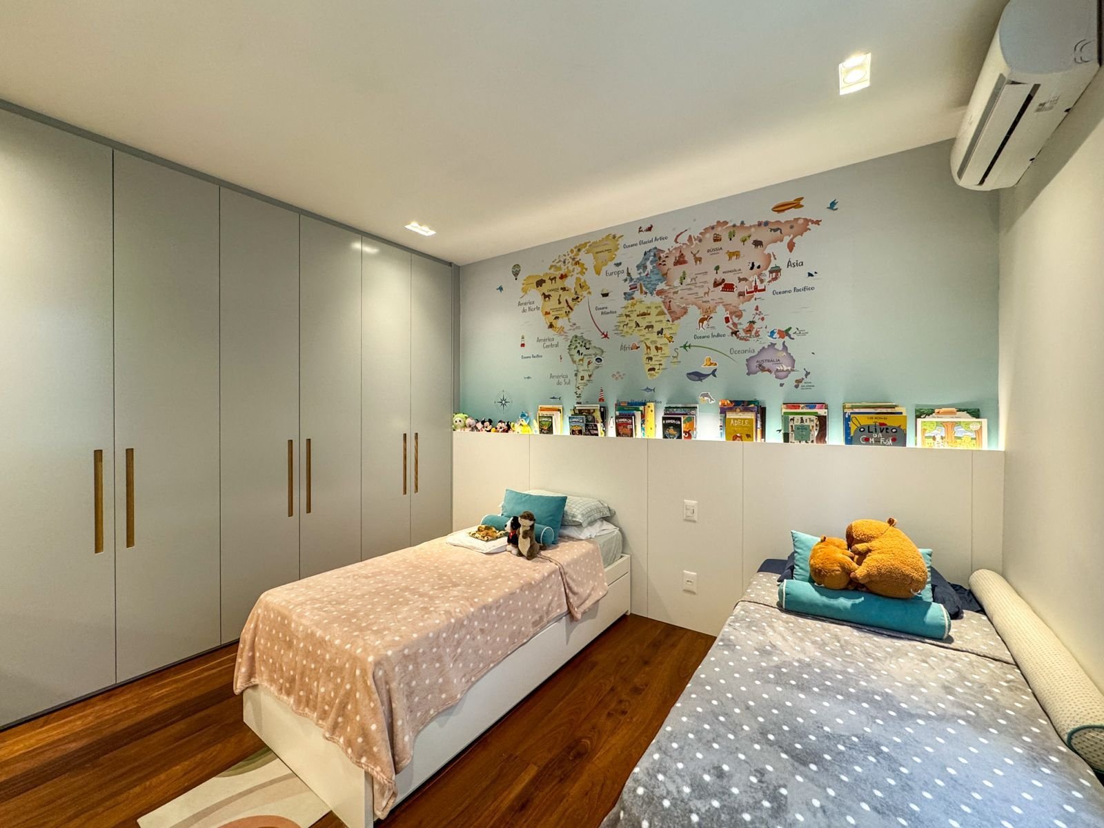 Cômoda de quarto infantil com espaço de armazenamento, paredes decoradas com mapa-múndi, camas com roupas de cama coloridas, tapetes confortáveis e brinquedos, ideal para ambientes infantis modernos e funcionais.