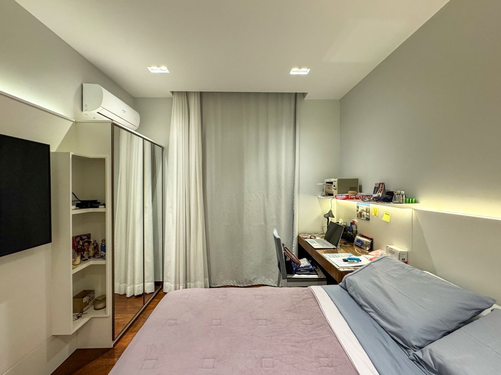 Conjunto de quarto confortável com cama de casal, escritório com computador, televisão, armário com espelho, ar-condicionado e cortinas brancas, ideal para hospedagem de negócios ou lazer.