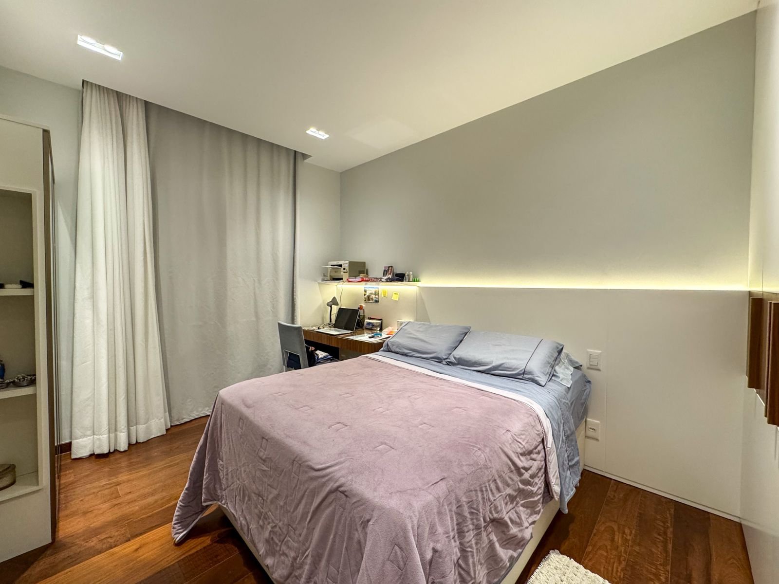 Suite moderna com decoração minimalista, iluminação embutida e piso de madeira, ideal para hospedagem confortável, com espaço para trabalho e descanso.