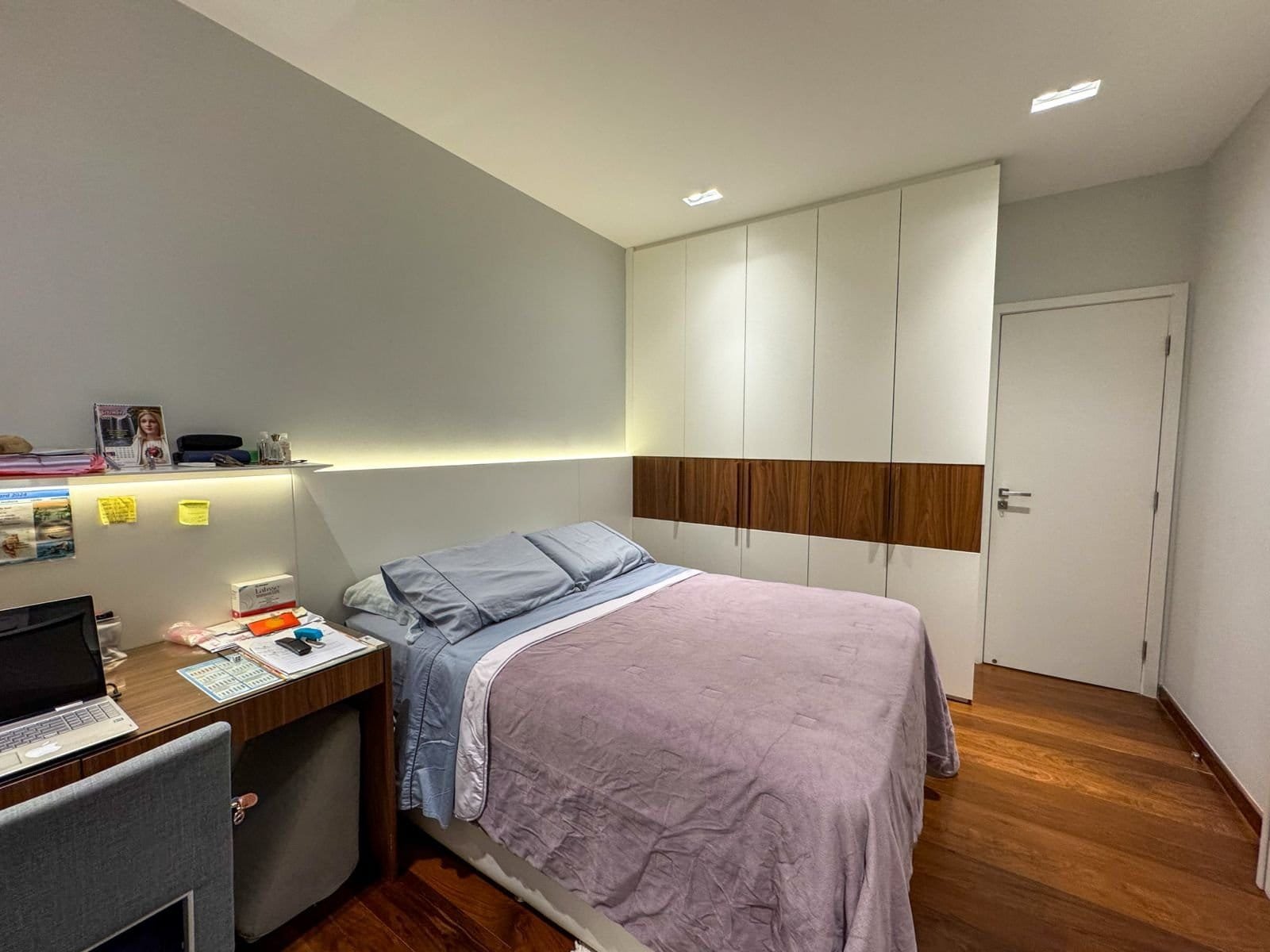 Cama de casal com cabeceira moderna em quarto de hotel elegante, iluminação suave, armários planejados de alta qualidade e detalhes sofisticados, ambiente confortável e bem decorado.