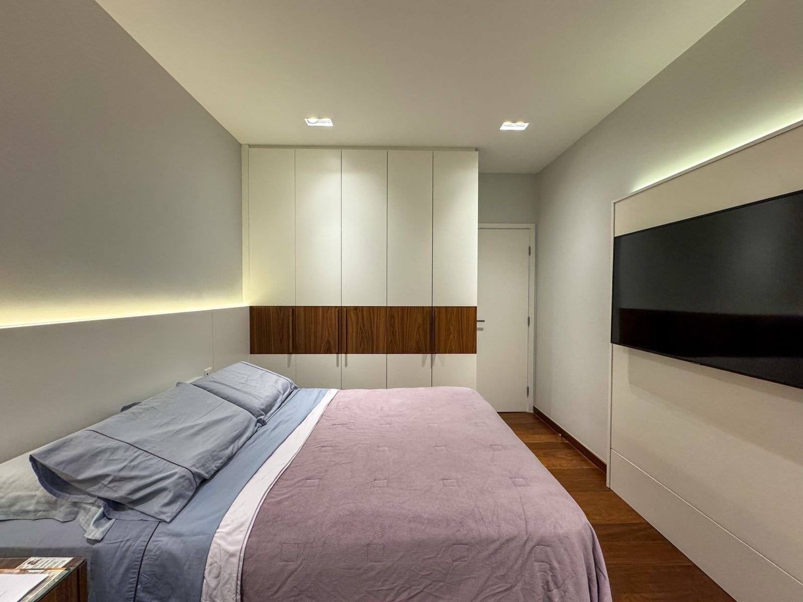 Confortável quarto de hotel com cama king size, armário moderno e televisão de tela plana, decoração elegante com iluminação suave, ideal para hospedagem de negócios ou lazer.