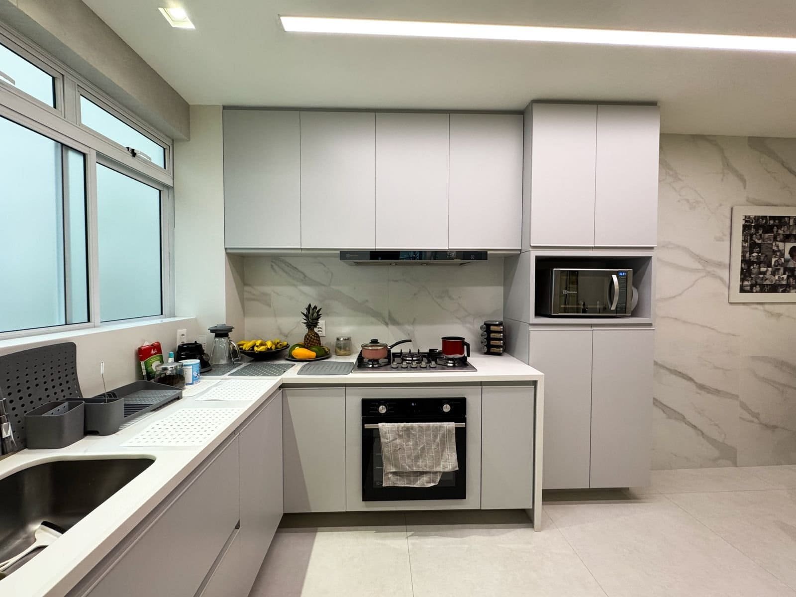 Moderno cozinha planejada com móveis brancos, eletrodomésticos embutidos e detalhes de mármore na parede, ideal para ambientes sofisticados e funcionais.
