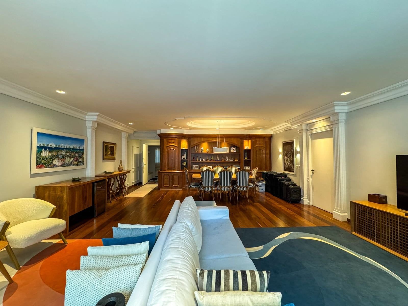 Conjunto de sala de estar com decoração elegante, móveis de madeira, sofá branco, tapete azul com detalhes brancos, iluminação sofisticada e detalhes clássicos, ideal para ambientes residenciais de alto padrão.