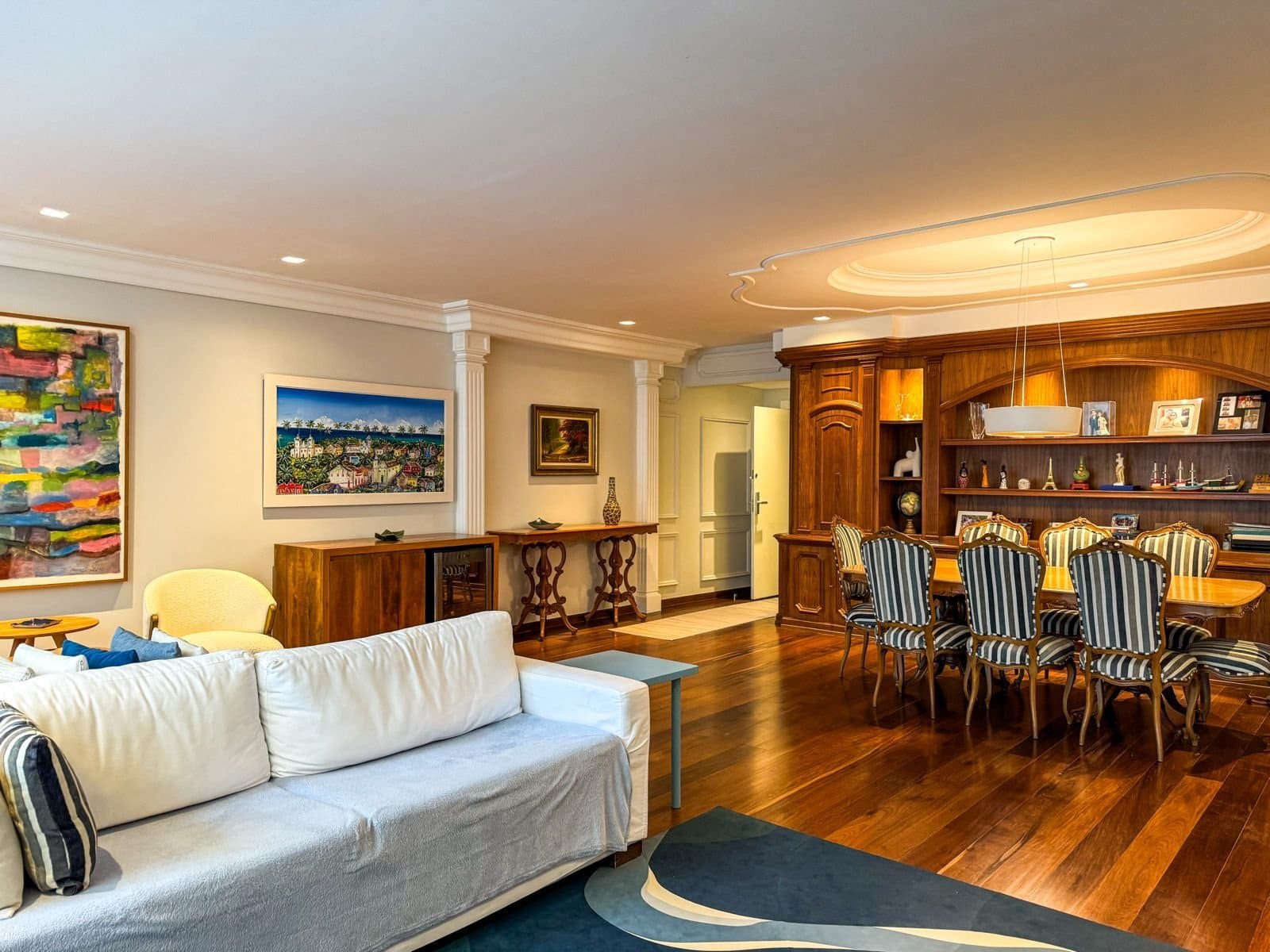 Elegante sala de estar e jantar de apartamento de alto padrão com móveis de madeira, obras de arte, iluminação moderna e detalhes sofisticados, criando um ambiente acolhedor e refinado.