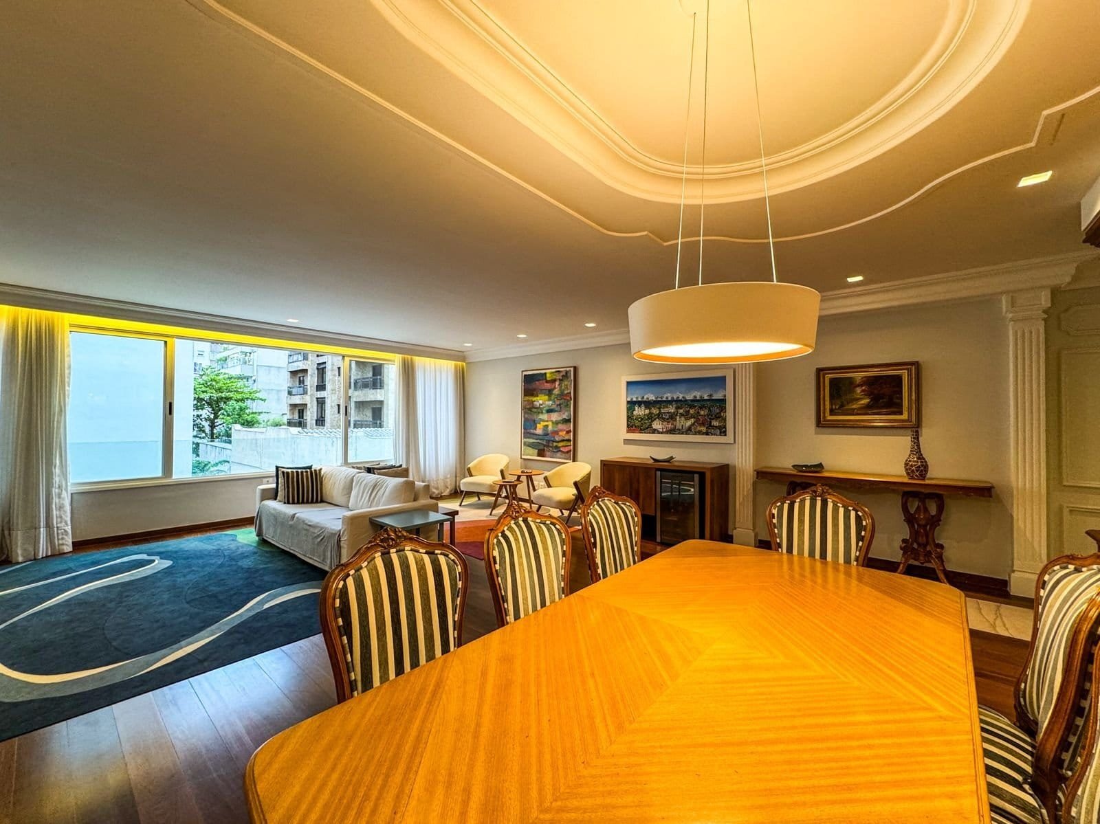 Luxuoso apartamento decorado com móveis clássicos, sala de estar espaçosa com janelas grandes, iluminação moderna e obras de arte, ideal para hospedagem de alto padrão no Grupo Monaco.