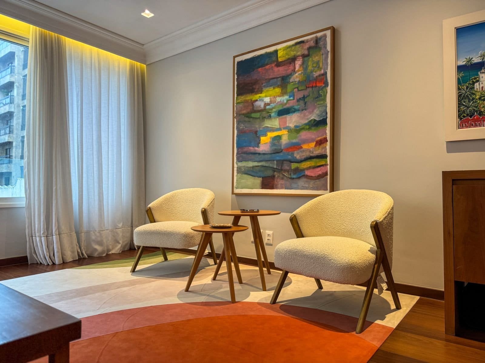 Elegante ambiente de sala de estar com duas poltronas de design confortável, quadros contemporâneos e cortinas brancas, em um espaço sofisticado e acolhedor de hotel ou residência de alto padrão.