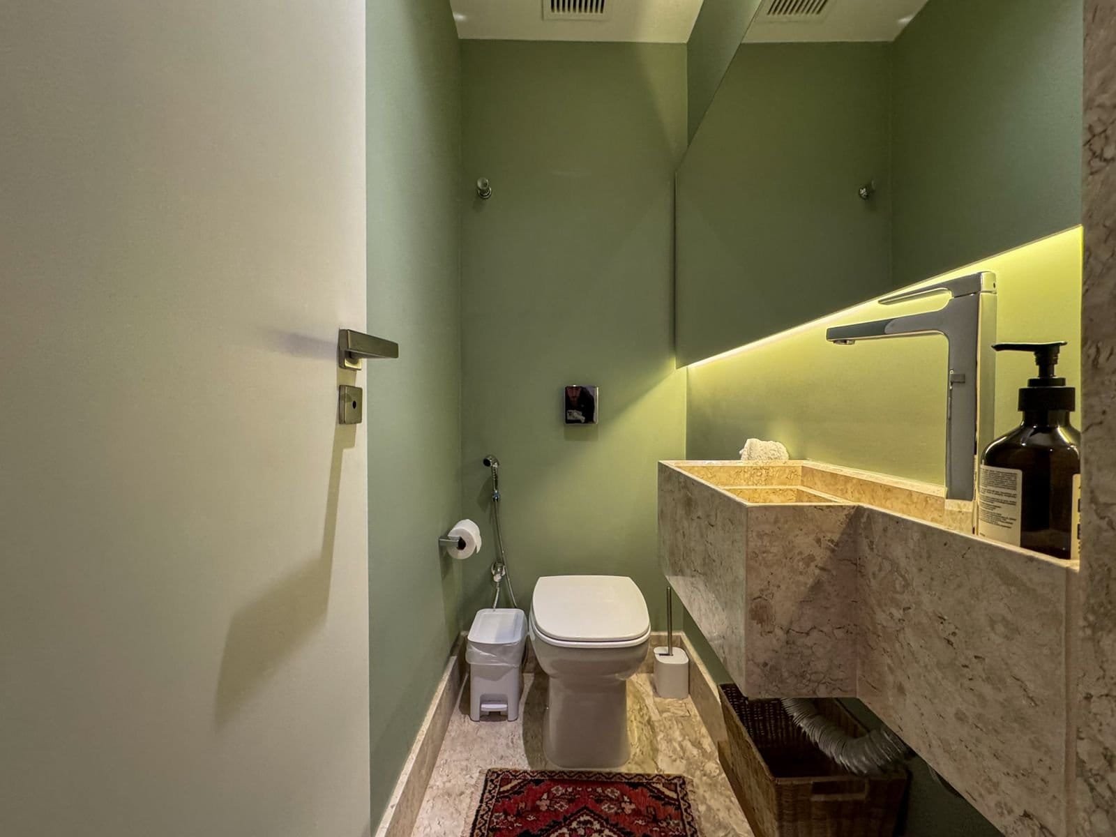 Conjunto de banheiro com parede verde, pia de granito e torneira moderna, ambiente clean e bem iluminado, com detalhes em mármore e acessórios funcionais.